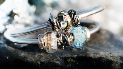 2 Silver bangles laying on a wet rock with glass beads and 4 silver spacers